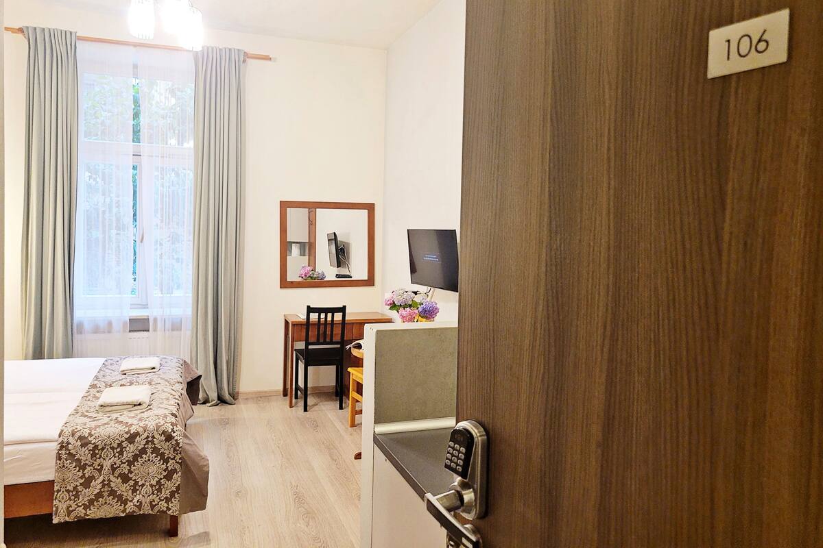 Camera d'albergo con un letto, una scrivania con una sedia, una TV e una porta con un numero.