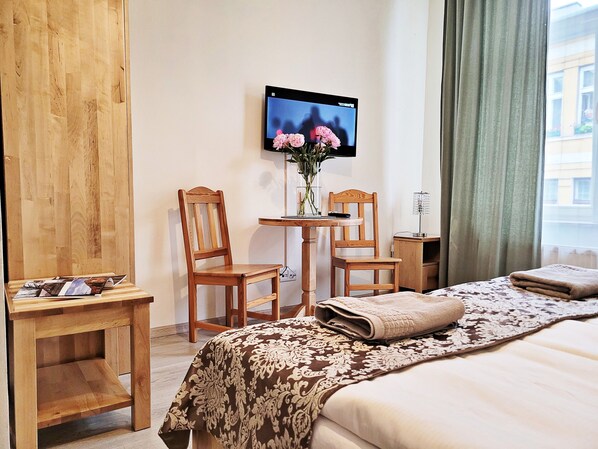 A hotel room with a bed, two wooden chairs, a small table with a vase of flowers, a television on the wall, and a window with curtains. - DReAM Post Aparthotel (Kraków)