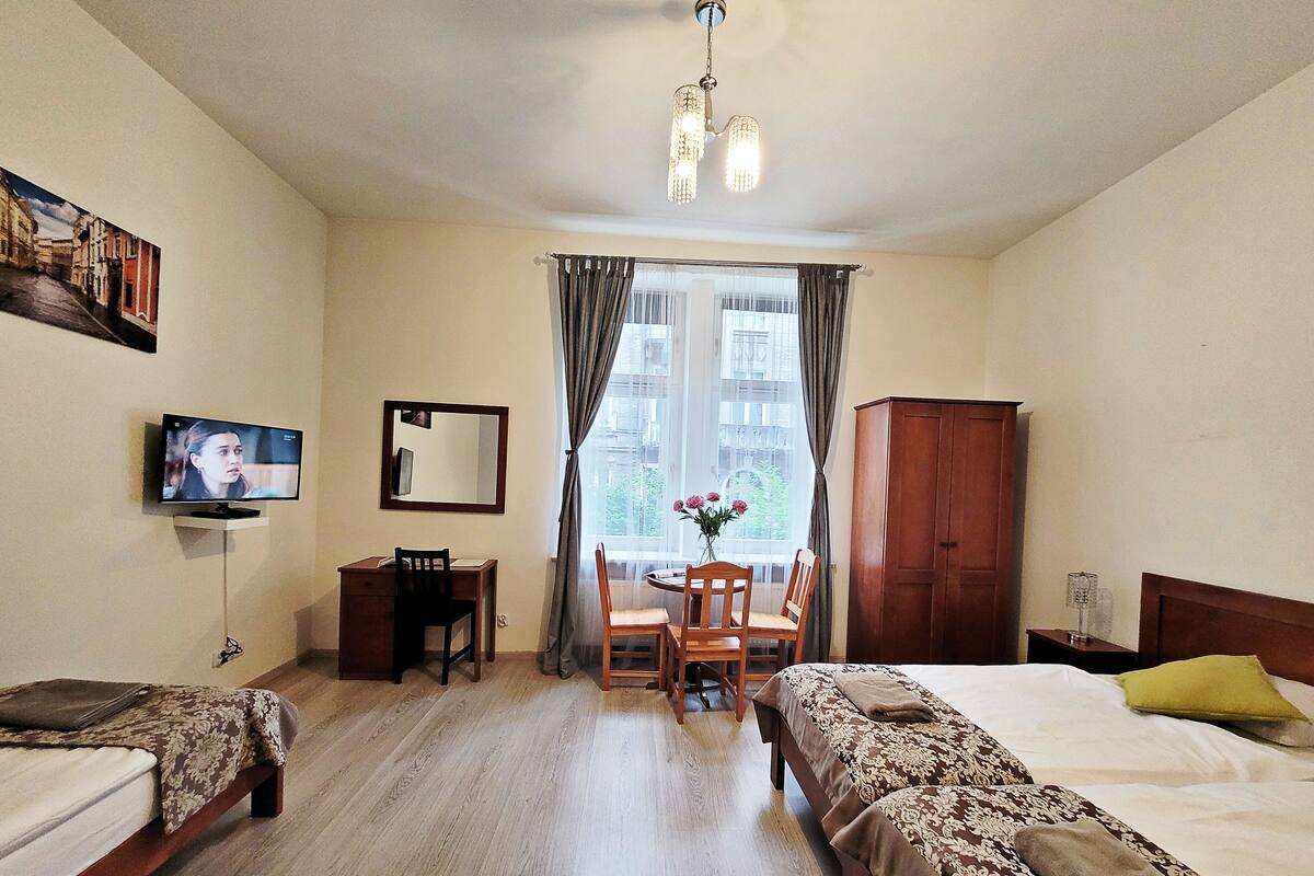 Una camera d'albergo con due letti, una scrivania, una sedia, una televisione, un armadio e una finestra con tende.