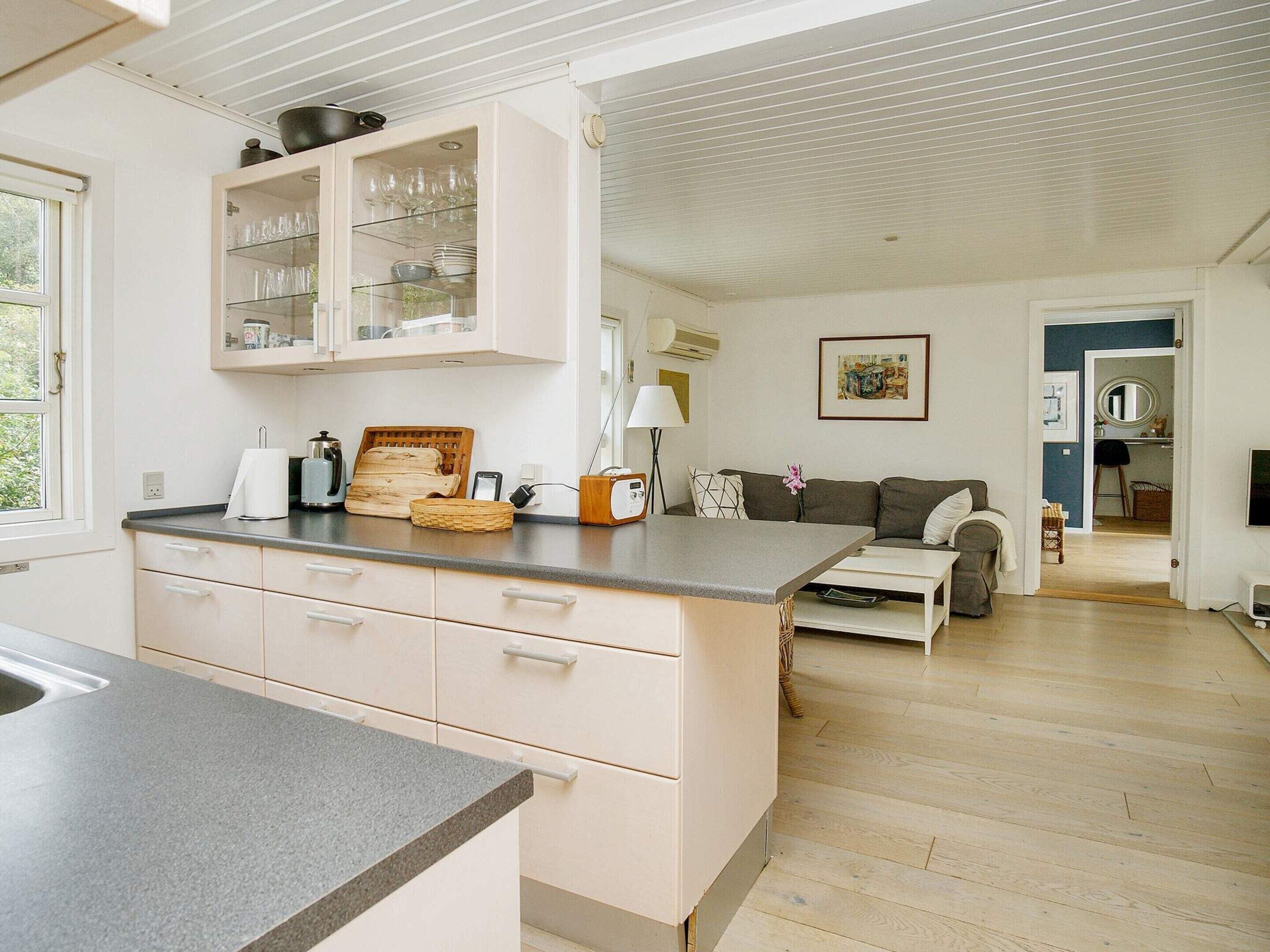 Et moderne køkken med en central ø, et spiseområde med en sofa og udsigt til et soveværelse.