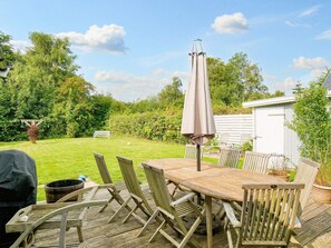 A wooden deck with a table and chairs, a barbecue grill, and a shed in a garden setting. - 10 Person Holiday Home in Graested (Graested)