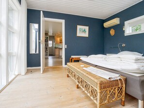 A bedroom with a bed, a wicker bench, a wall-mounted air conditioner, and a door leading to a kitchen. - 10 Person Holiday Home in Graested (Graested)