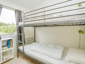 Un letto a castello con una scaletta, uno scaffale con dei libri e una finestra con tende.