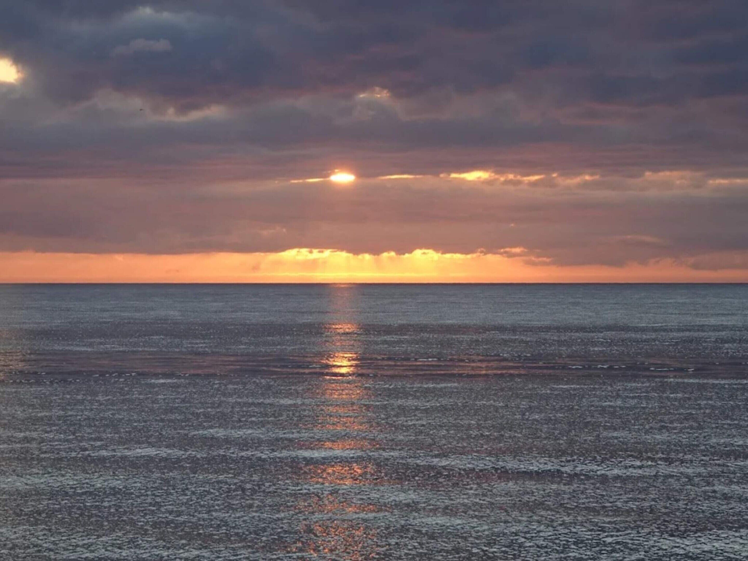 A calm sea at sunset with a clear horizon.