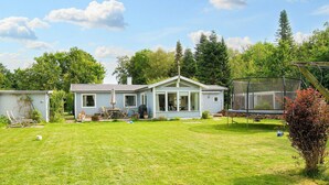 Ein Bungalow mit großem Vorgarten, Trampolin und überdachter Sitzgelegenheit.