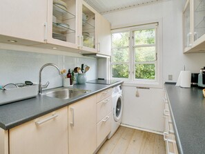 A modern kitchen with a built-in washing machine, a large window, and a countertop with various kitchen items. - 10 Person Holiday Home in Graested (Graested)