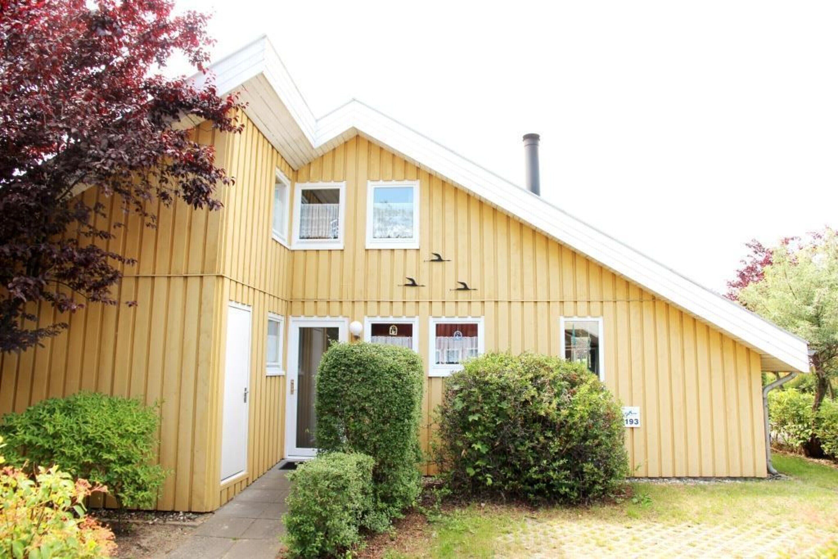 Un bâtiment en bois jaune, doté d’un toit en pente, d’une cheminée et d’un petit porche avec une porte.