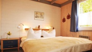 A bedroom with a bed, bedside tables, a wall-mounted shelf, and a window with curtains. - Ferienhaus im Skandinavischen Stil (Mirow)