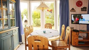 A dining area with a round table, wooden chairs, a cabinet, and a television. - Ferienhaus im Skandinavischen Stil (Mirow)