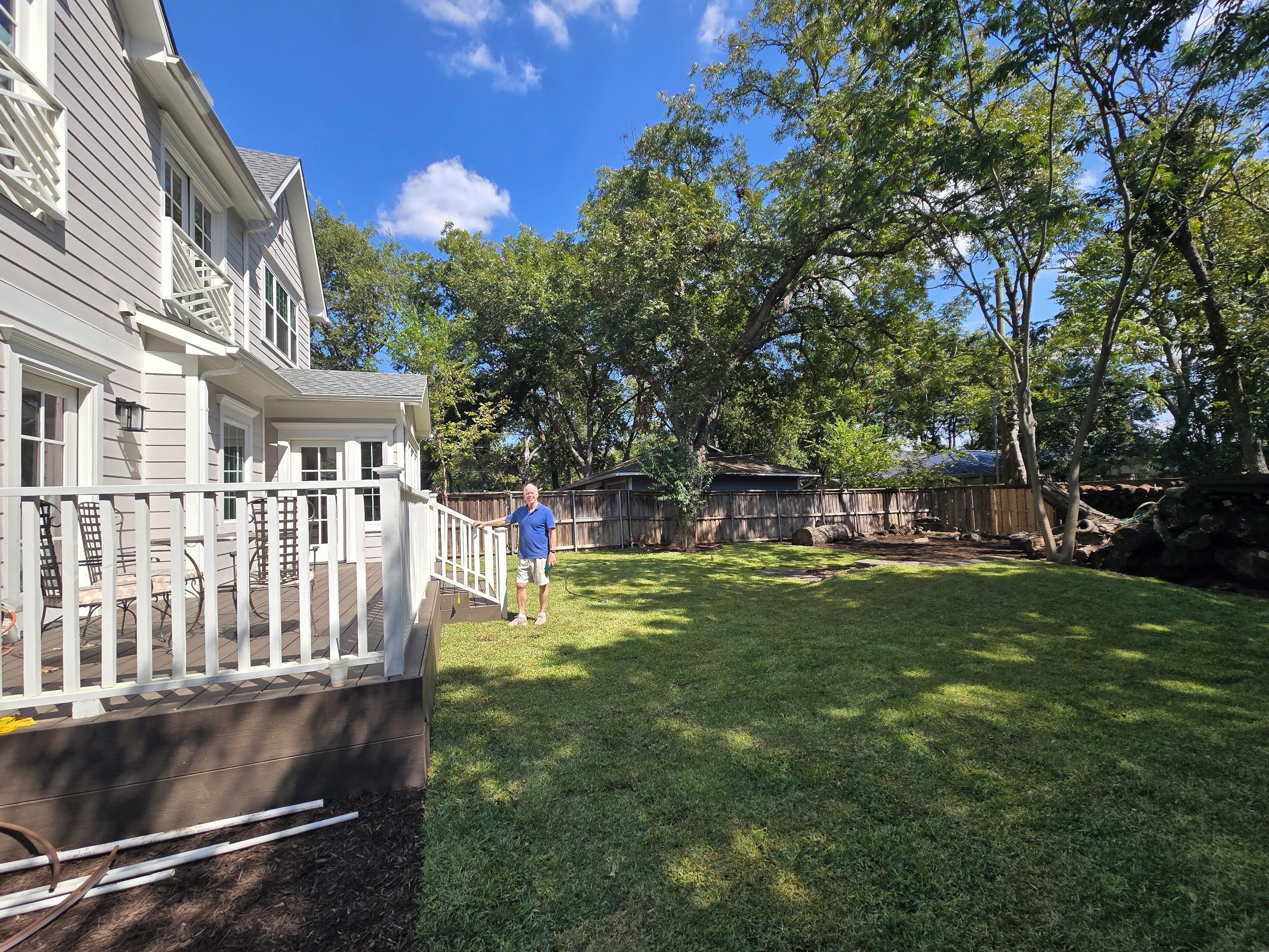 A residential backyard with a wooden deck, a white fence, and a wooden fence in the background.