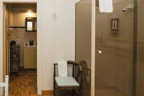 A small, compact room with a shower, a chair, and a sink. - Historic Farm Cottage | Hawke's Bay Station (Maraetotara)