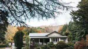 Une maison de plain-pied avec un porche à l ’avant, entourée d’arbres et d’une pelouse.
