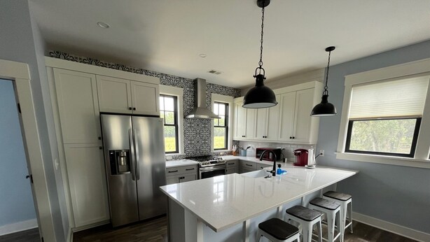 Una cocina moderna con armarios blancos, electrodomésticos de acero inoxidable, una isla grande con taburetes y una ventana que proporciona luz natural.