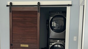 Un lavadero con dos lavadoras y secadoras apiladas, una puerta corredera y una encimera blanca.