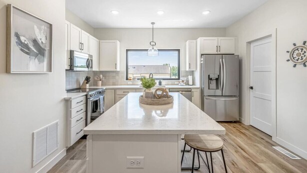 A modern kitchen with white cabinetry, a central island, stainless steel appliances, and a large window providing natural light.