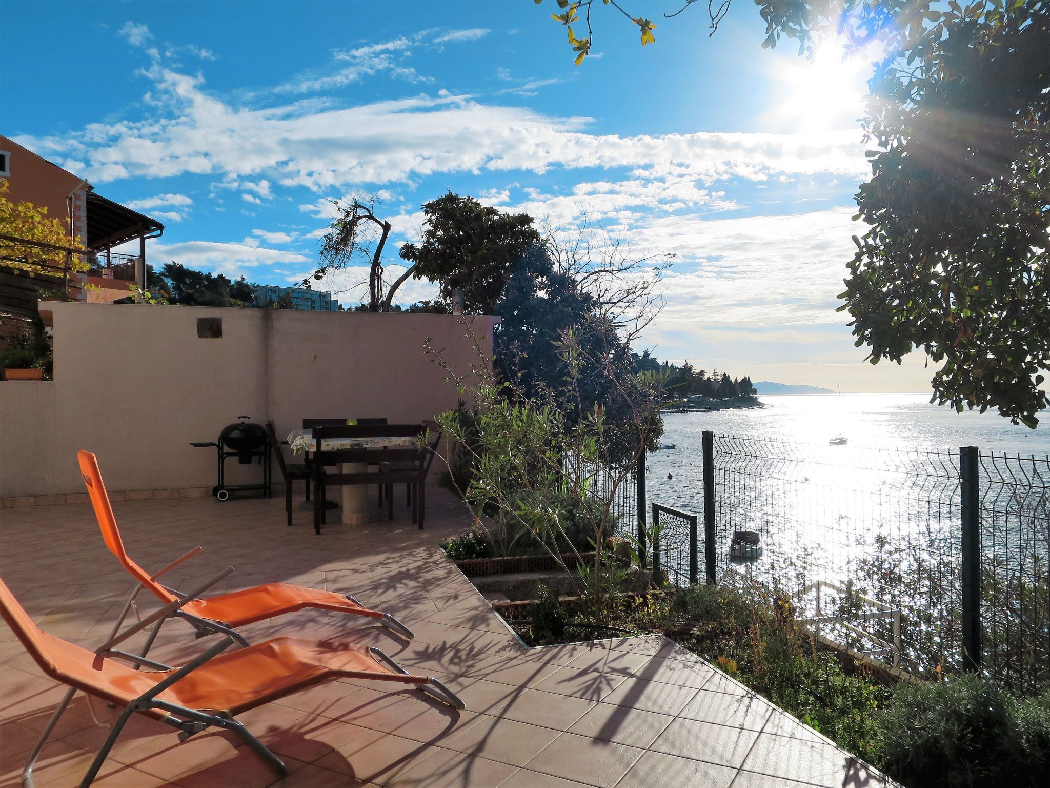 An outdoor patio with a view of the sea, a grill, and orange chairs.