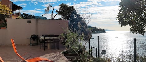 An outdoor patio with a view of the sea, a grill, and orange chairs.