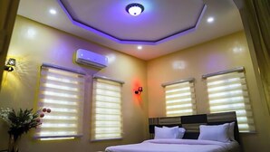 Een hotelkamer met een bed, twee ramen met zonwering, een airconditioning en een plafondlamp.