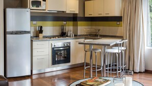 Cocina moderna con refrigerador, microondas, horno y taburetes de bar. Hay una mesa de comedor con un libro y vasos.