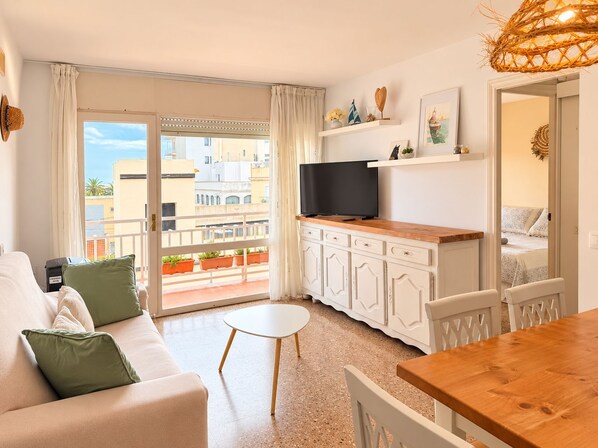 A modern apartment with a balcony, a flat-screen TV, a dining area, and a kitchenette.