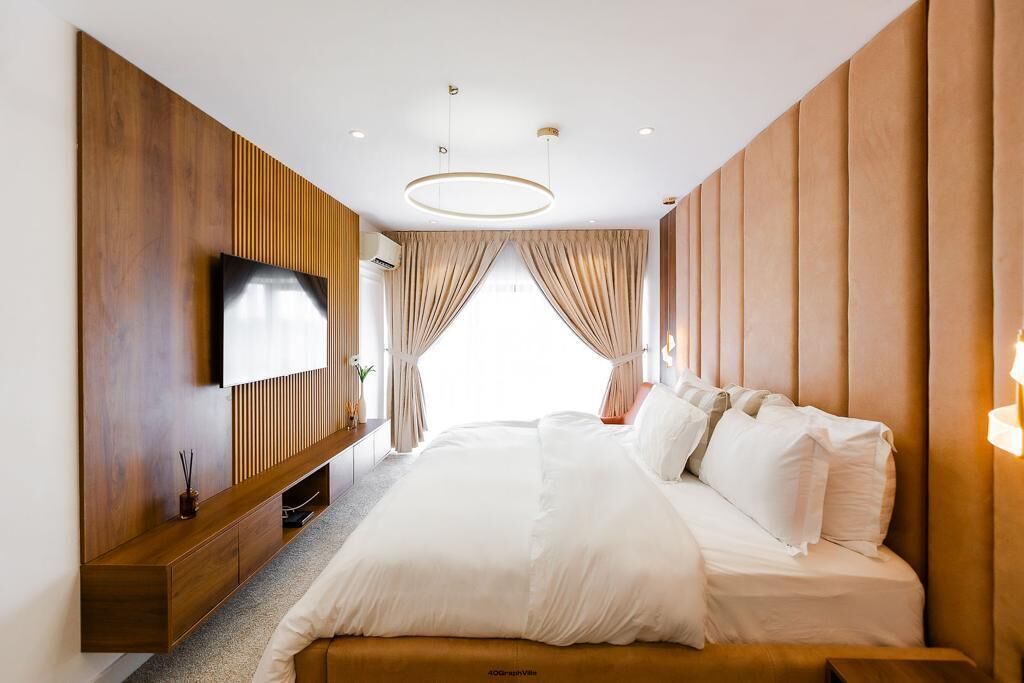 Habitación de hotel moderna con una cama grande, paneles de madera, un televisor de pantalla plana y un gran ventanal con cortinas.
