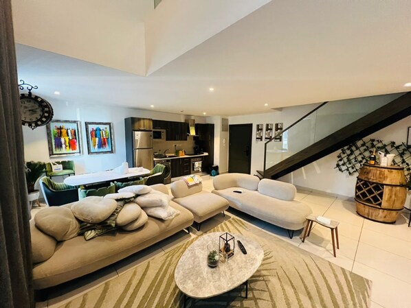 A modern living room with a sectional sofa, a round coffee table, and a staircase leading to an upper level. - Prime properties executive two bedroom (Accra)