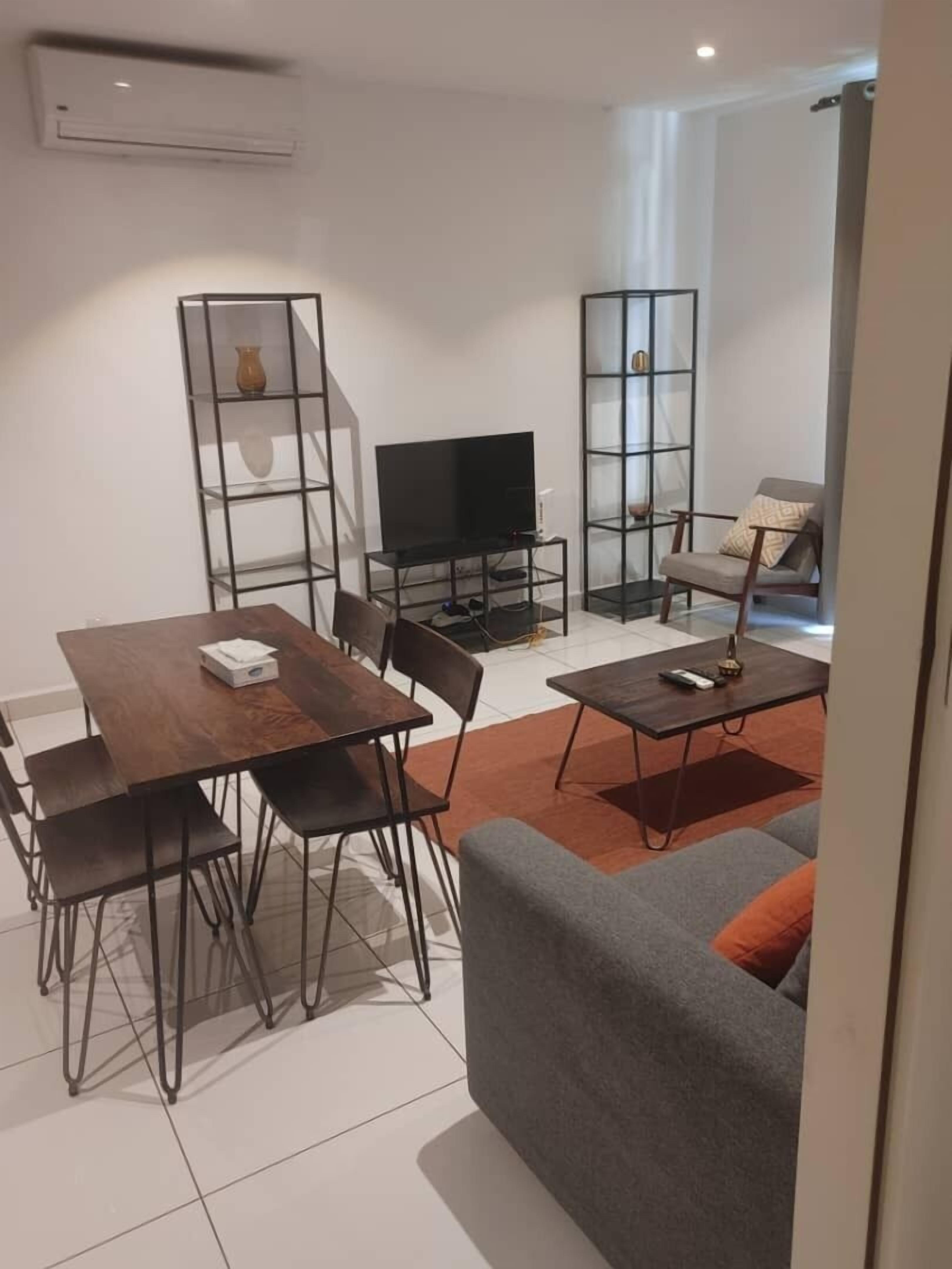 A modern living room with a dining area, a grey sofa, a TV, and a bookshelf.