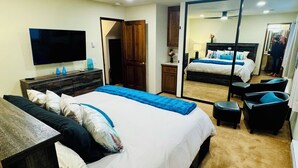 A modern bedroom with a large bed, a TV, a ceiling fan, and a mirror.