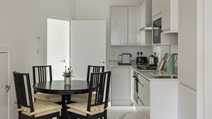 A modern kitchen with white cabinets, a dining table with chairs, and a small island. - Picktheplace Kensington Lux Apartments (London)
