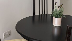 A round dining table with a potted plant, two cushioned chairs, and a wall socket. - Picktheplace Kensington Lux Apartments (London)