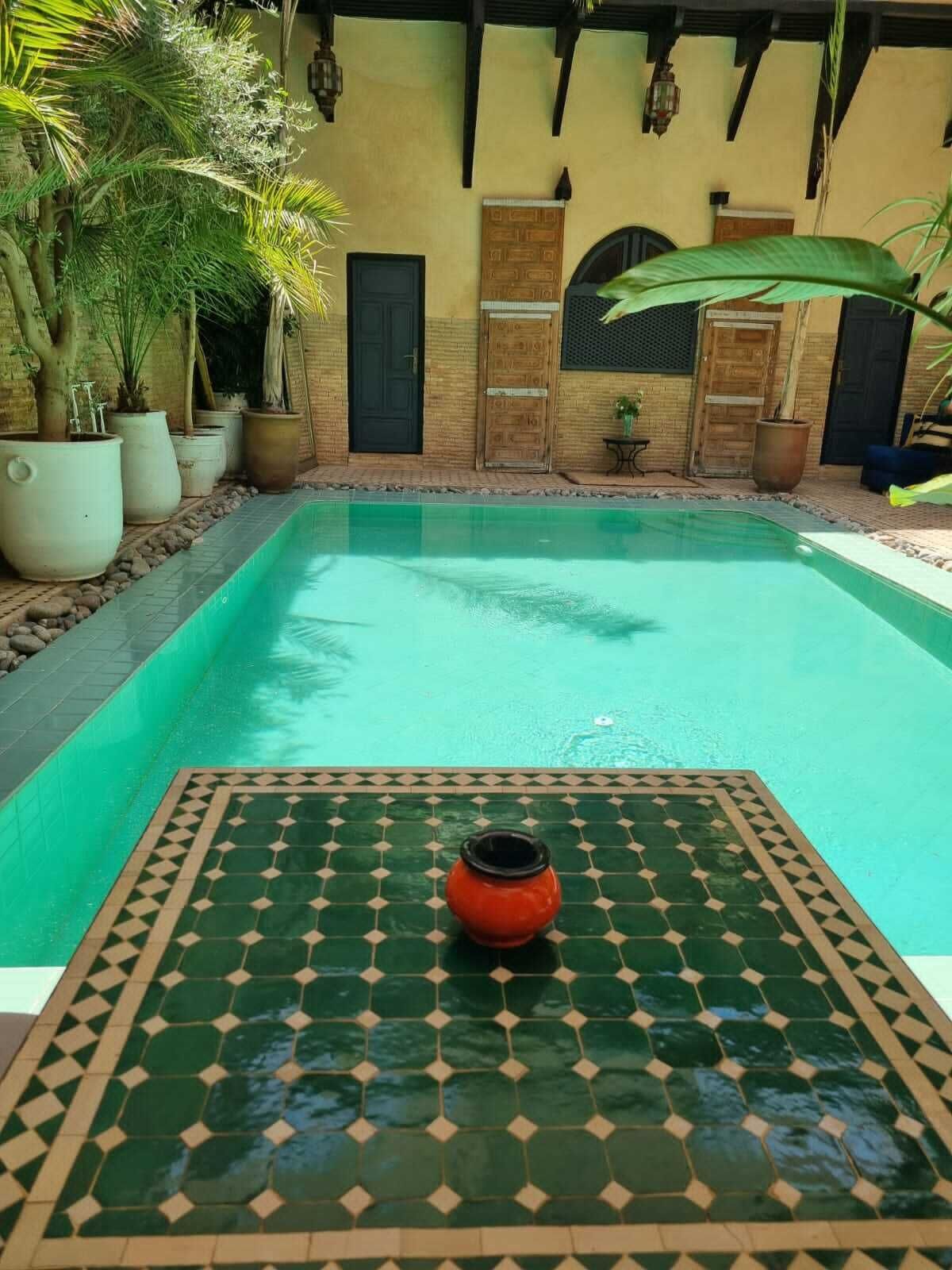 A swimming pool with a tiled floor and a decorative pot in the foreground.