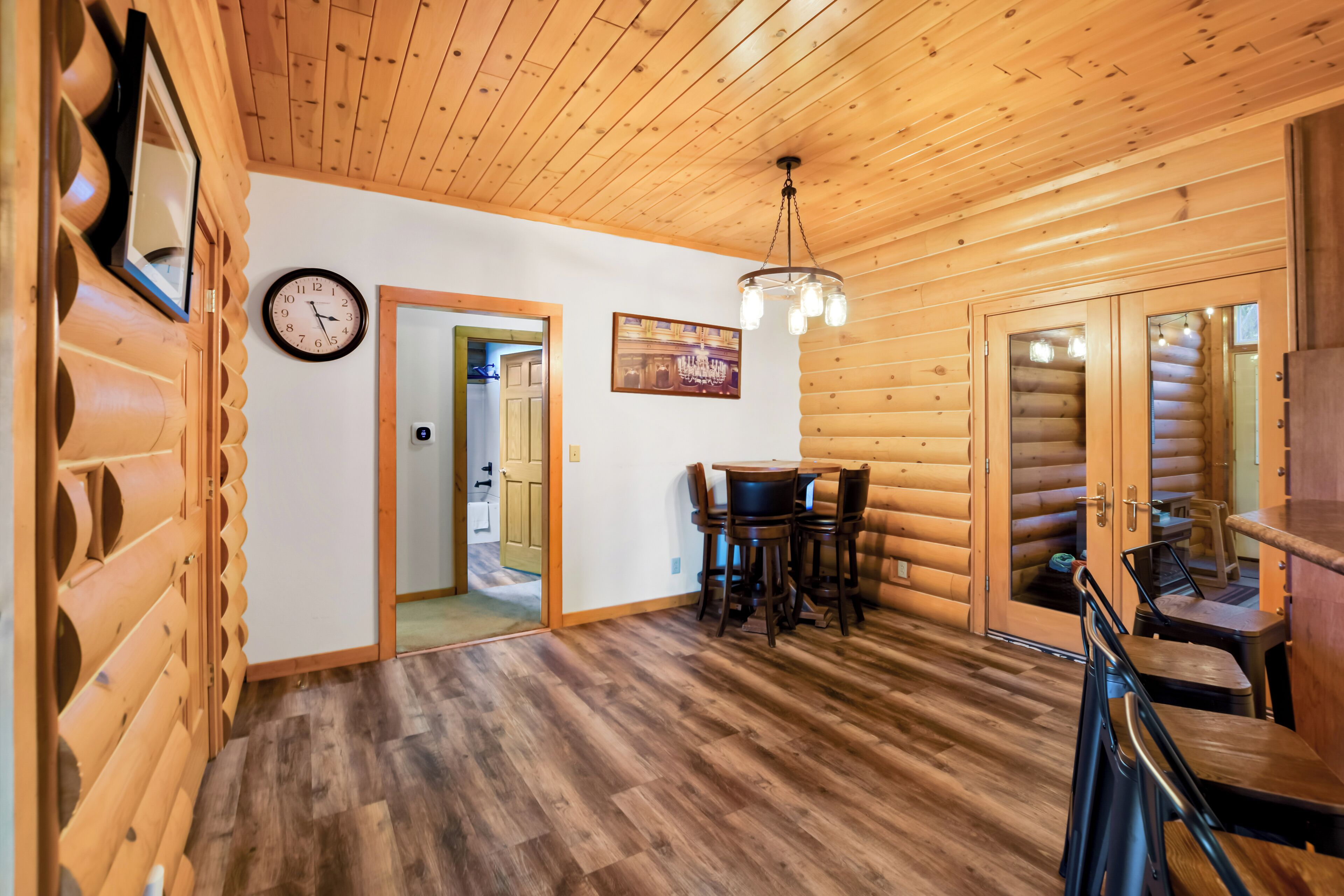 A wooden interior with a dining area, a clock, and a framed picture on the wall.