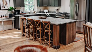 Una cocina moderna con armarios oscuros, una isla grande con taburetes de bar, un refrigerador de acero inoxidable y piso de madera.