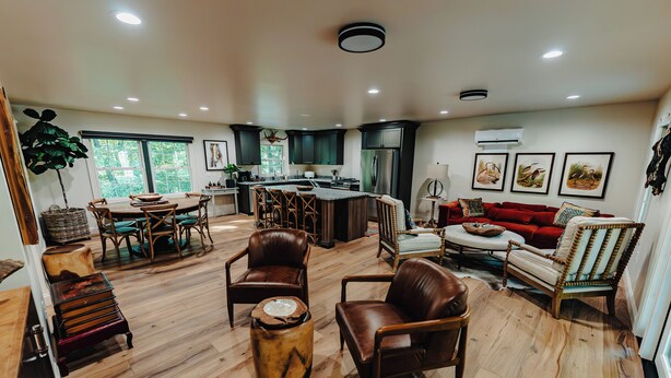 Un salón comedor amplio con piso de madera, un área de comedor con una mesa grande y una cocina con alacenas oscuras y un refrigerador.