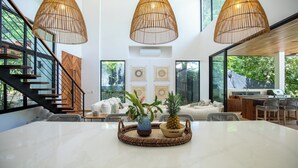 Un vaste espace dédié à la salle à manger, avec une grande table, des chaises en osier et un îlot central doté d’un barbecue.