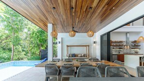 Un espace repas moderne avec vue sur la piscine, un plafond en bois et des meubles en osier.