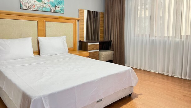 A hotel room with a large bed, a wooden headboard, a flat-screen TV, a small armchair, and a large window with sheer curtains. - City Blue Hotel (Elazig)