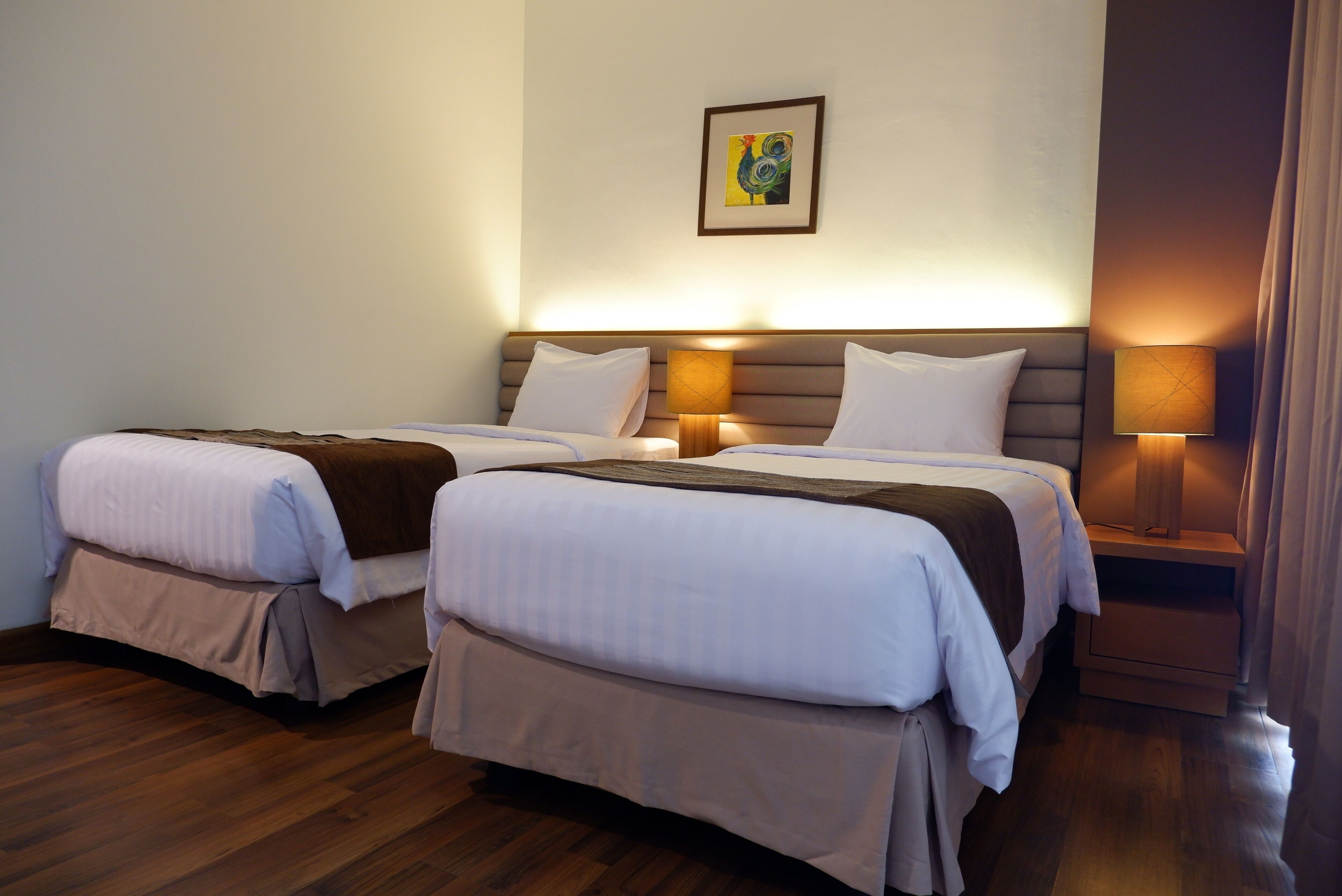 Camera d'albergo con due letti, pavimento in legno e un quadro incorniciato appeso al muro.