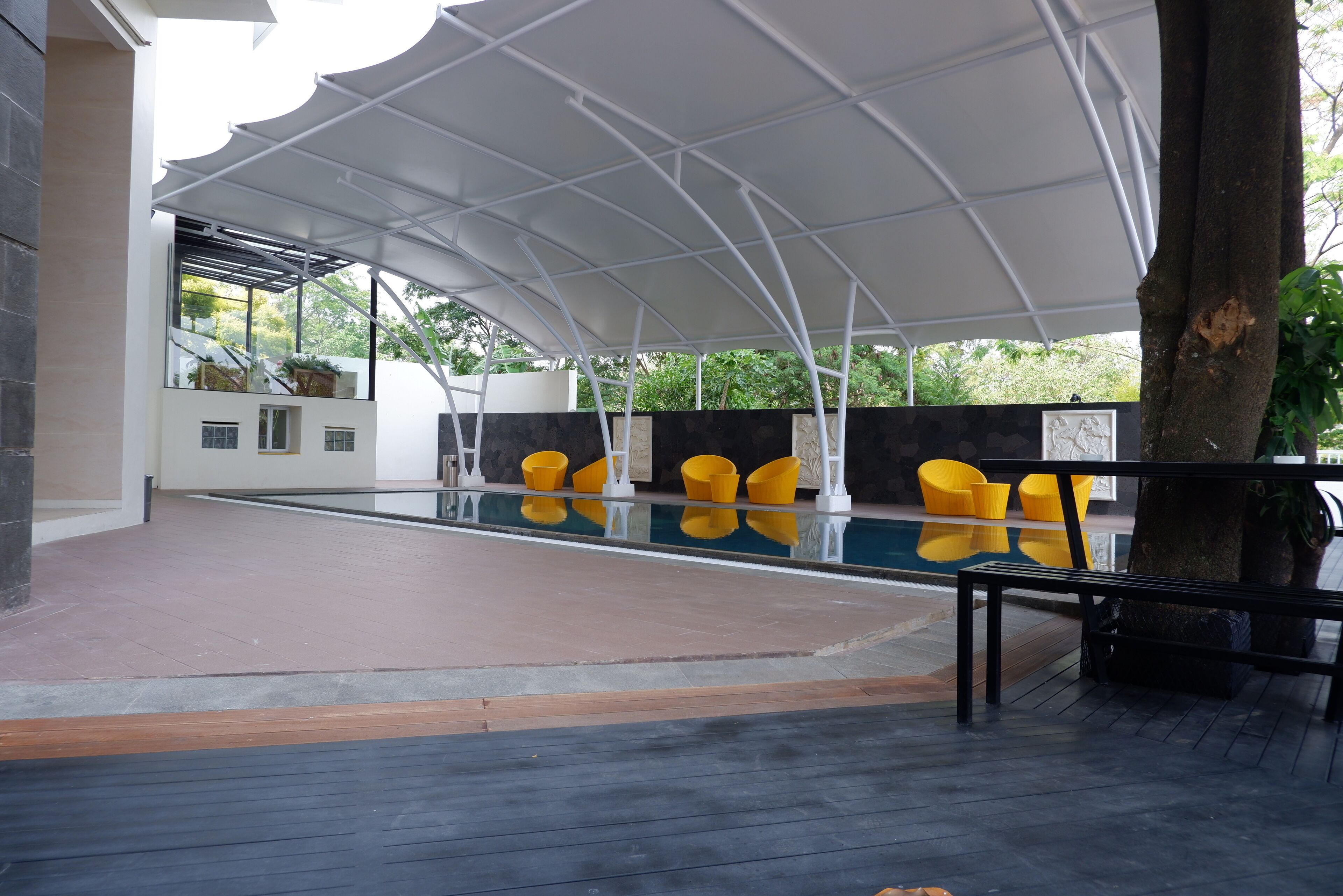 A covered outdoor swimming pool area with yellow chairs and a modern architectural design.