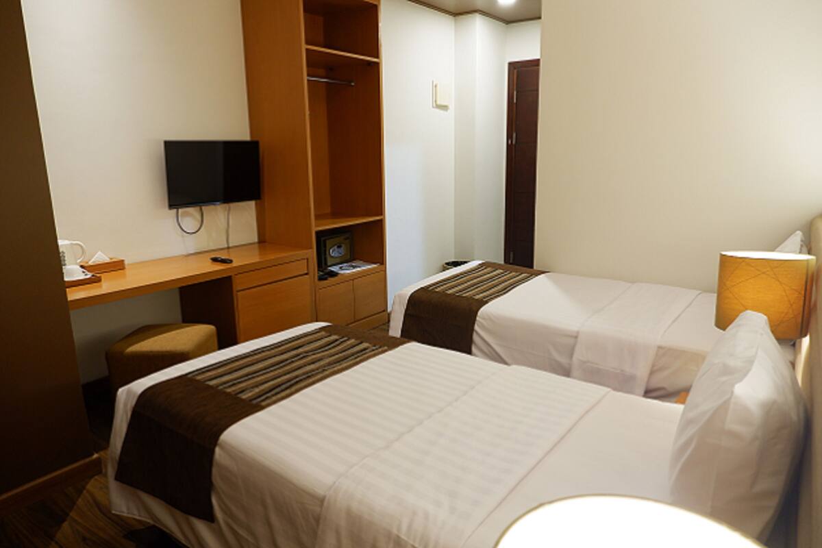 A hotel room with two beds, a desk with a television, a wardrobe, and a bedside lamp.