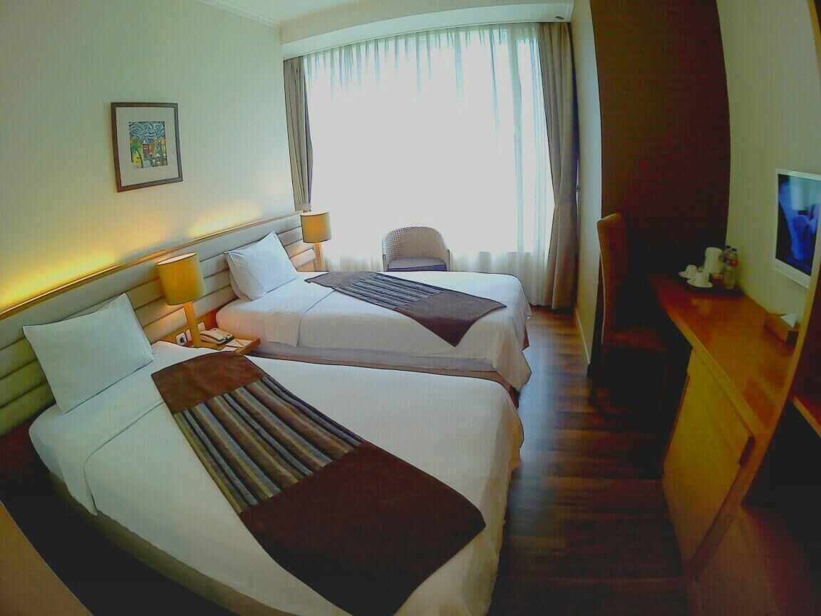 A hotel room with two beds, a desk, a chair, and a television.