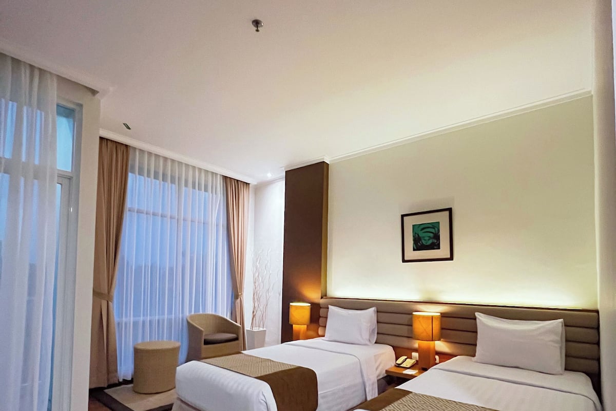 A hotel room with two beds, a sitting area, and a large window with curtains.