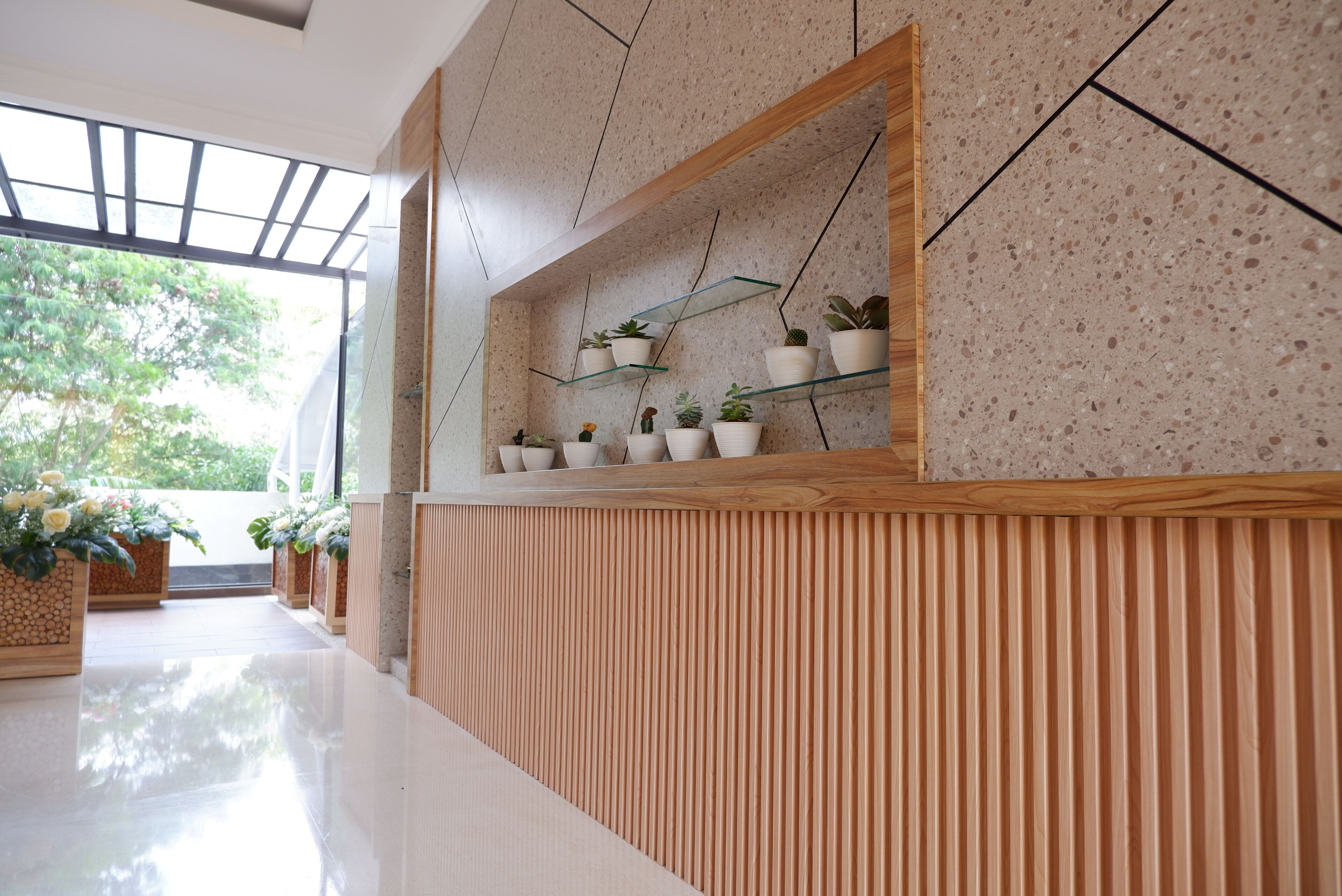 A modern interior with a wooden panel wall, a glass shelf with potted plants, and a view of greenery outside.