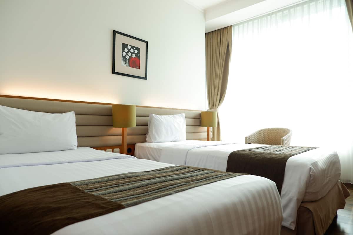 A hotel room with two beds, a framed artwork on the wall, and a chair.