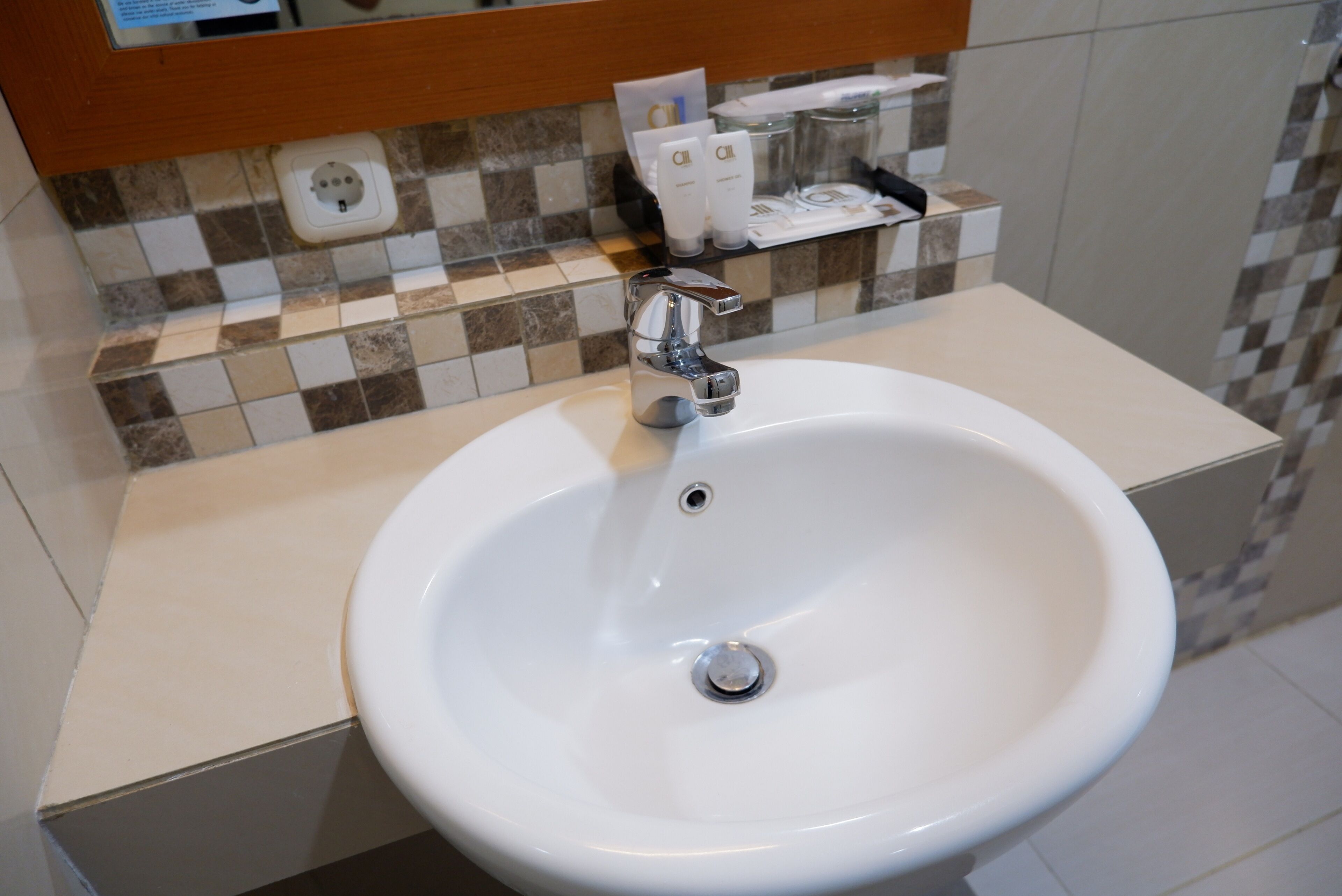 A bathroom sink with a chrome faucet, a mirror above it, and toiletries on a shelf.