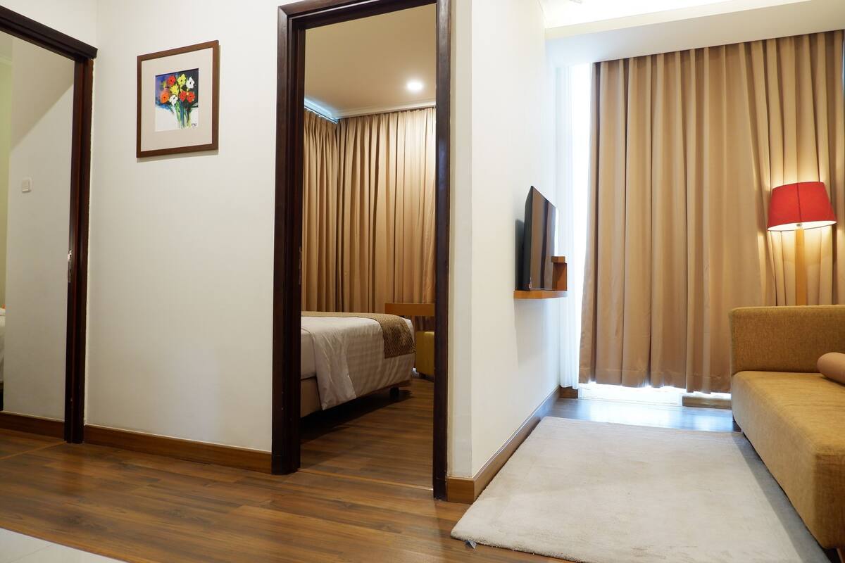 A hotel room with a bed, a sofa, a TV, and a painting on the wall.