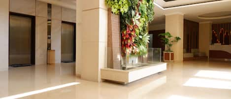 A modern lobby with a polished floor, a vertical garden, and a reception area with a seating arrangement.