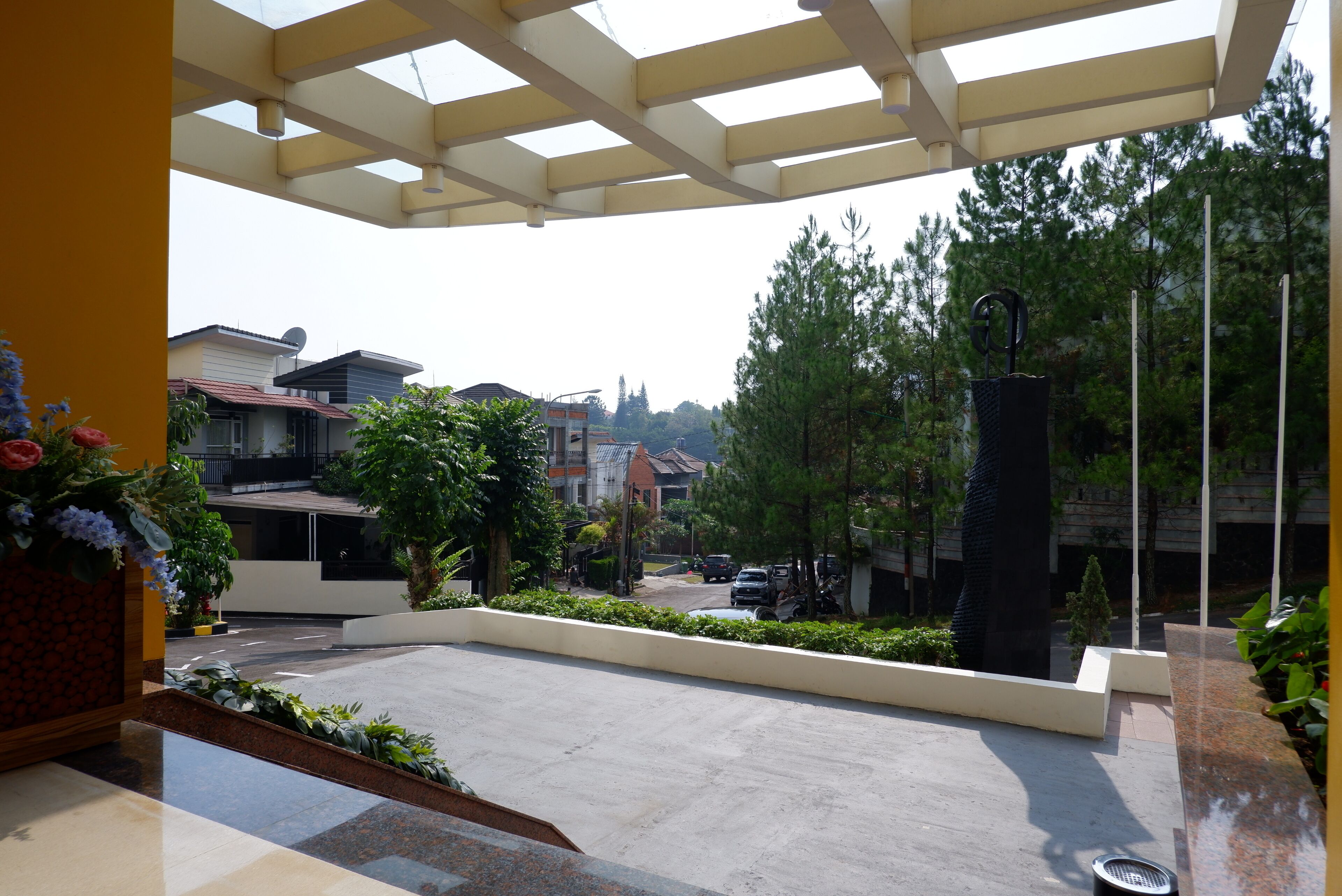 A covered outdoor area with a concrete floor, surrounded by greenery and residential buildings.