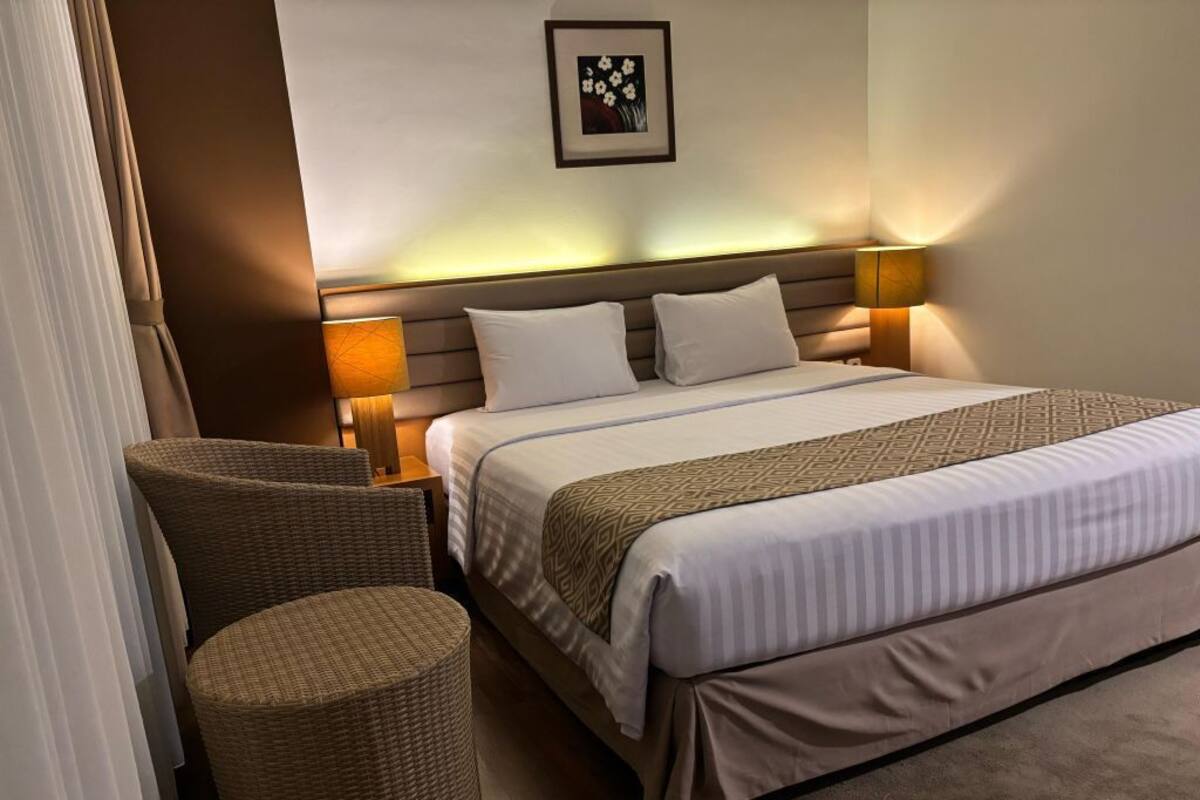 A hotel room with a large bed, two bedside lamps, a headboard, and a small round table.