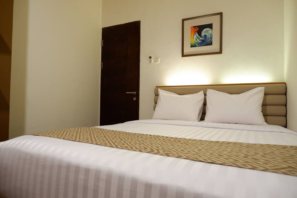 A neatly made bed with a patterned bedspread, a headboard, and a framed picture on the wall.